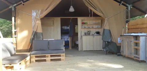 Interno di tenda safari con divano in pallet, cucina in legno e scaffali, atmosfera accogliente.