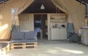 Safari telt interiør med sofa, køkken og spiseområde i naturligt træ, hyggelig og rustik stemning.