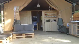 Innenraum eines Safari-Zeltes mit Holzsofa, Küchenzeile und Regalen, gemütlich und rustikal.