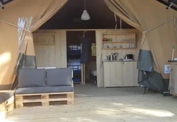 Intérieur d'une tente safari avec canapé, kitchenette en bois et étagères, ambiance chaleureuse.