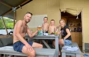 Een gezin geniet samen van eten en drinken aan een picknicktafel voor een safaritent op vakantie.