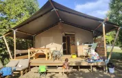 Photo d’une tente safari avec terrasse en bois, mobilier d’extérieur, jouets et un jeune enfant devant.