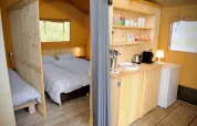 Interno di una tenda safari con camera da letto e angolo cucina in legno chiaro, ben attrezzato e luminoso.