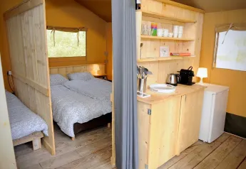 Interno di una tenda safari con camera da letto e angolo cucina in legno chiaro, ben attrezzato e luminoso.