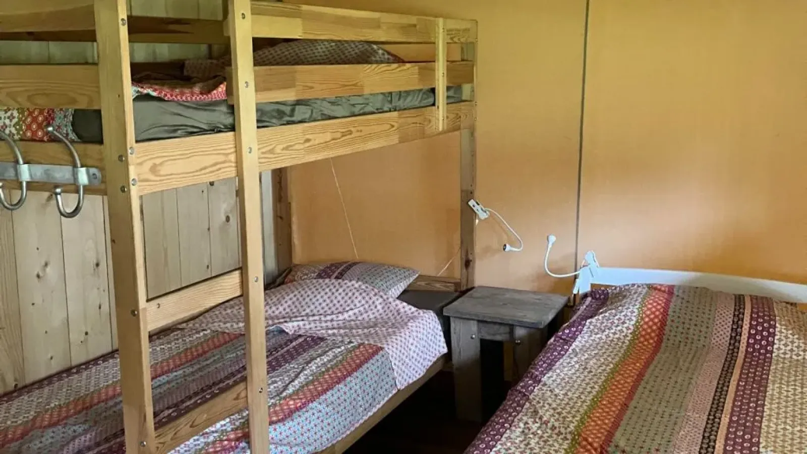 Interieur van een safaritent met stapelbed en eenpersoonsbed, beide voorzien van kleurrijk beddengoed.