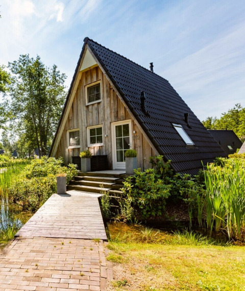 Casa pequeña tipo A Wellness Lodge en Hof van Salland, rodeada de vegetación y un estanque en Holanda.