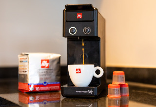 Cafetera con cápsulas y taza illy sobre encimera de cocina en alojamiento glamping, lista para usar.