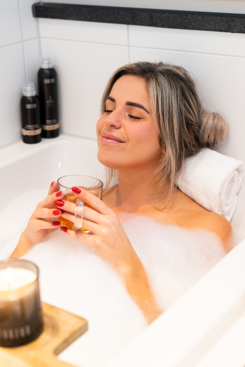 Mujer relajándose en un baño de burbujas con una bebida en Wellness Lodge, Hof van Salland, Países Bajos.