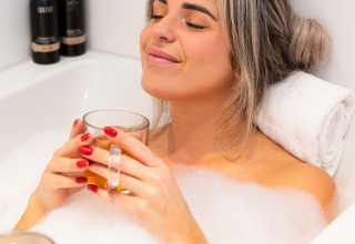 Mujer relajándose en un baño de burbujas con una bebida en Wellness Lodge, Hof van Salland, Países Bajos.
