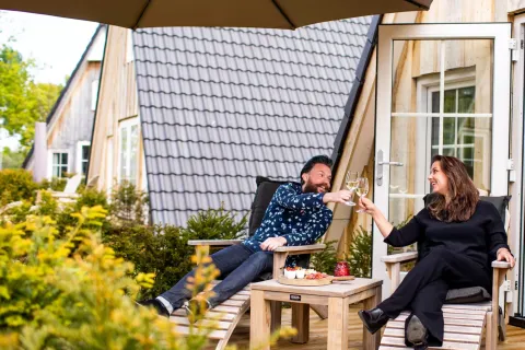 Pareja brindando con vino y aperitivos en la terraza de Wellness Lodge en Hof van Salland, Países Bajos.