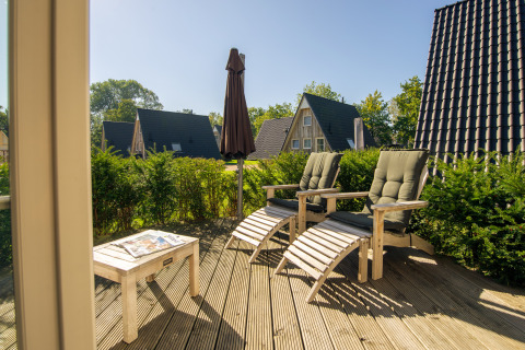 Terraza soleada con tumbonas y vista a casas pequeñas en Wellness Lodge, Hof van Salland, Países Bajos.