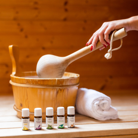 Scène de sauna avec main, seau en bois, louche et huiles essentielles en glamping, ambiance relaxante.