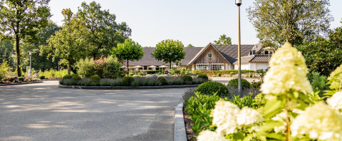 Entrée d’un hébergement glamping de luxe entouré d’arbres, massifs fleuris et jardins soigneusement entretenus.