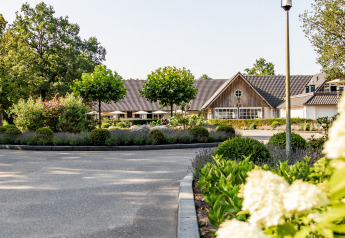 Entrée d’un hébergement glamping de luxe entouré d’arbres, massifs fleuris et jardins soigneusement entretenus.
