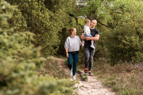Une famille se promène sur un sentier forestier près de son hébergement glamping, entourée de verdure.