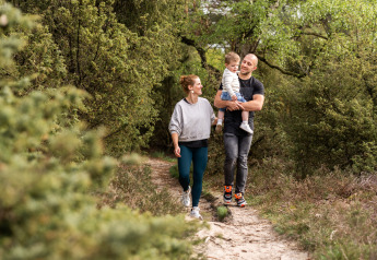Une famille se promène sur un sentier forestier près de son hébergement glamping, entourée de verdure.