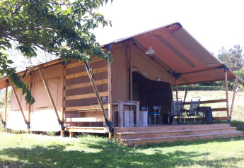 Safari tent at Campsite Podere sei Poorte in Italy with wooden porch, outdoor seating and green surroundings.