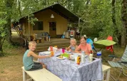 Famille prenant un repas à une table de pique-nique devant une tente safari lors d’un séjour en forêt.