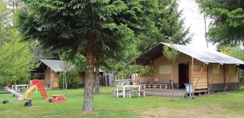Tente safari dans un cadre naturel avec aire de jeux et arbres, idéale pour des vacances familiales.
