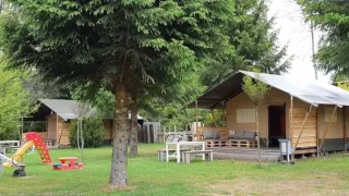 Tente safari dans un cadre naturel avec aire de jeux et arbres, idéale pour des vacances familiales.