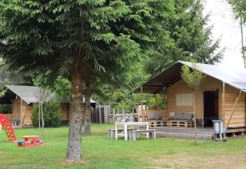 Safari tent in a natural setting with a playground and trees, ideal for family trips and relaxation.