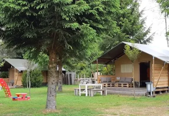 Safari tent in a natural setting with a playground and trees, ideal for family trips and relaxation.
