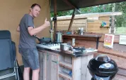 Mand laver mad i udendørskøkken ved safari telt, giver tommelfinger op og smiler afslappet.