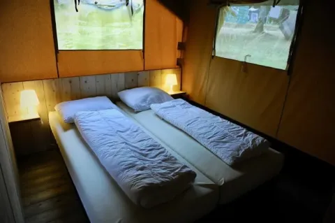 Interior view of a safari tent with two single beds, soft lighting, wooden floor and window views outside.