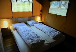 Interior view of a safari tent with two single beds, soft lighting, wooden floor and window views outside.