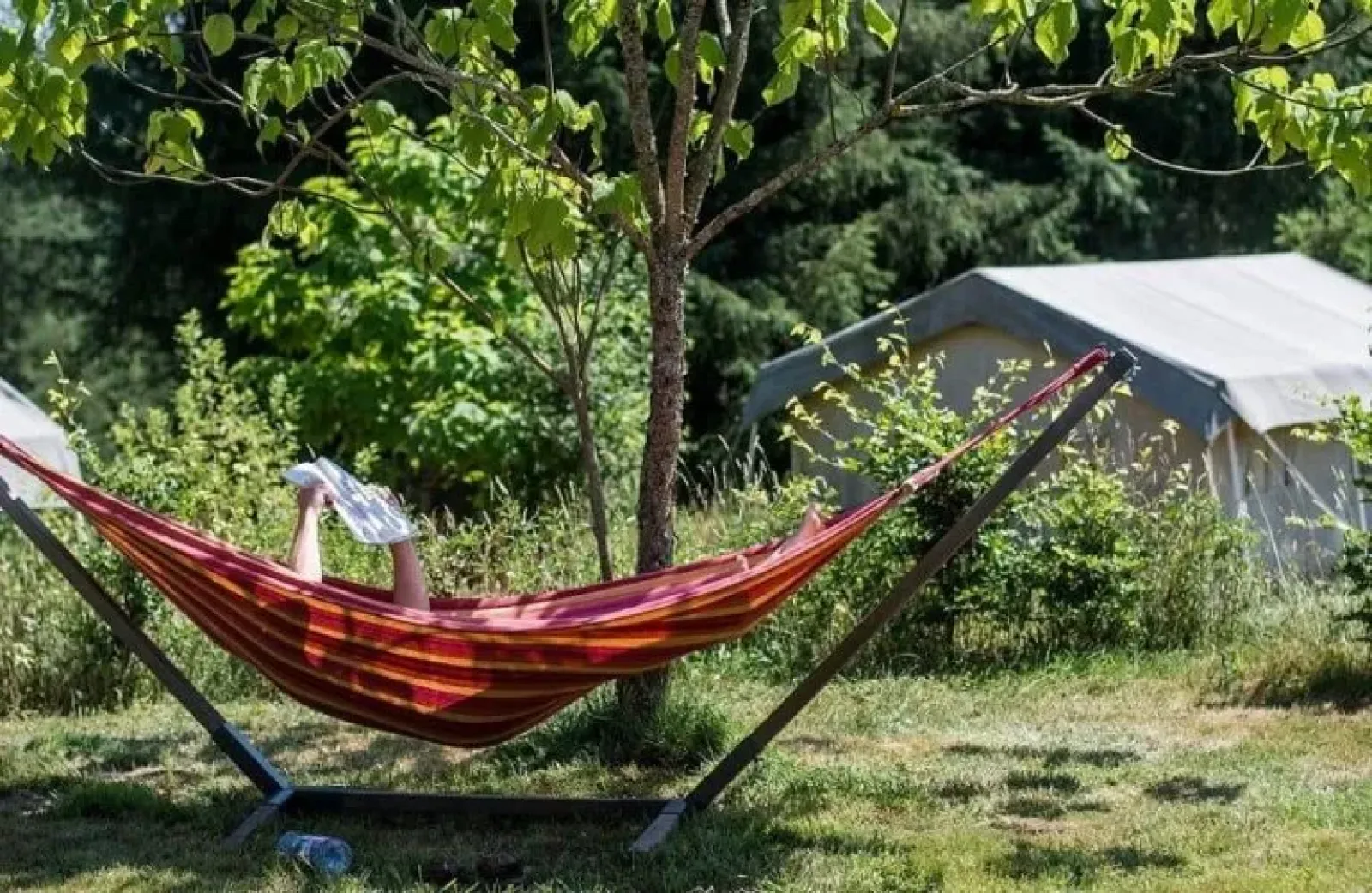 Een persoon ligt in een hangmat en leest een krant naast een safaritent in een groene omgeving.