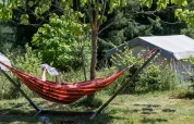 A person relaxes in a hammock reading a newspaper near a safari tent surrounded by lush greenery.