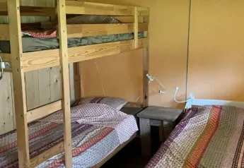 Habitación interior de una tienda safari con litera de madera, cama individual y colchas multicolores.