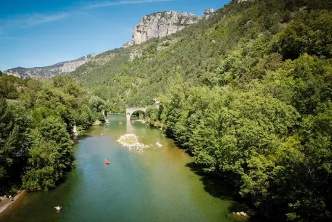 Fiume tra colline verdi e ponte di pietra nei pressi di Lanuéjols, Occitania, Francia, in una giornata soleggiata.