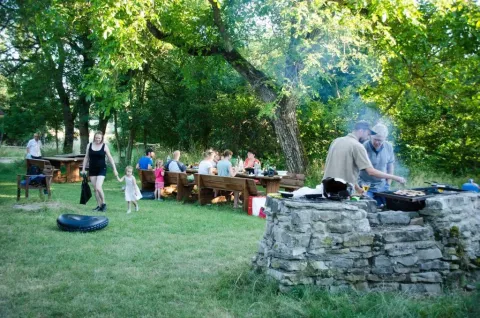 Mensen genieten van een barbecue in de zon bij Domaine de Pradines, omringd door bomen en houten tafels.