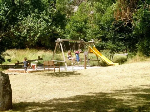 Kinder spielen auf einem Spielplatz mit Schaukel und gelber Rutsche im Domaine de Pradines, Occitanie, Frankreich.