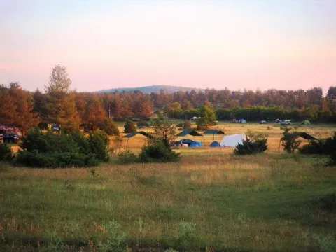 Zonsondergang bij Domaine de Pradines vakantiepark in Occitanie, Frankrijk, met tenten op een grasveld.