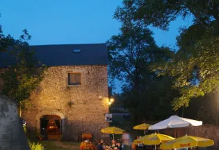 Evening view of rustic stone building and outdoor dining at Domaine de Pradines holiday park in Occitanie, France.