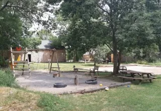 Parque infantil en Domaine de Pradines con columpios, arenero y mesas bajo árboles en Occitania, Francia.