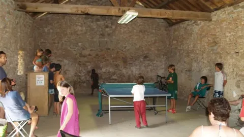 Children and adults play table tennis in a rustic stone room at Domaine de Pradines holiday park, Occitanie, France.