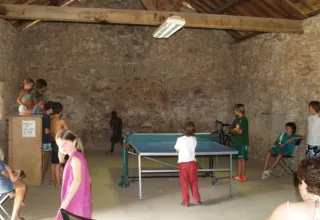 Kinder und Erwachsene spielen Tischtennis in einem rustikalen Steinraum im Ferienpark Domaine de Pradines, Occitanie.