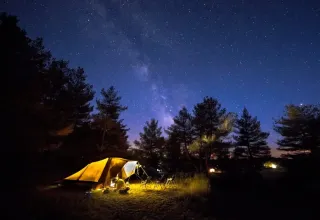 Camping en Domaine de Pradines con una tienda iluminada bajo el cielo estrellado en Occitania, Francia.