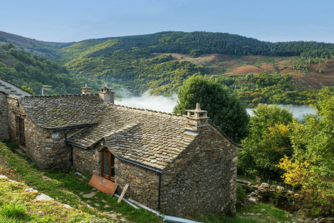 Maison en pierre au milieu des collines verdoyantes près de Lanuéjols, Occitanie, France, avec brume en vallée.
