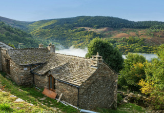 Stone house nestled among green hills near Lanuéjols, Occitanie, France, with mist in the valley below.