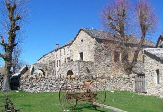 Casa de piedra y árboles en Domaine de Pradines, parque vacacional en Occitania, Francia, bajo cielo azul.