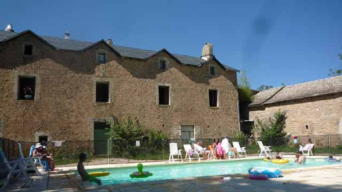 Feriegæster slapper af ved en swimmingpool foran en rustik stenbygning på Domaine de Pradines, Occitanie.