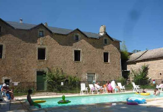 Feriegæster slapper af ved en swimmingpool foran en rustik stenbygning på Domaine de Pradines, Occitanie.