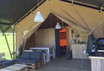Vue intérieure d’une tente safari avec meubles en bois, coin cuisine, et espace détente confortable.