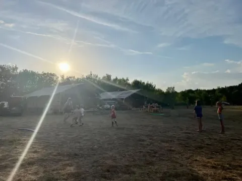 Kinder spielen vor Safarizelten auf Domaine de Pradines in Frankreich, die Sonne scheint durch die Bäume.