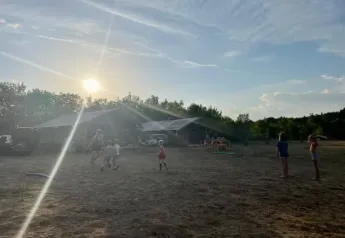 Des enfants jouent près d’une tente safari au Domaine de Pradines en France, sous un soleil couchant.