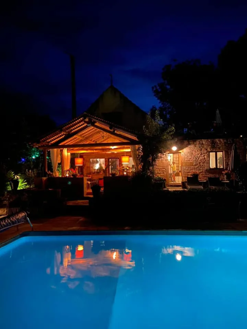 Cabina illuminata accanto alla piscina di notte al campeggio Mas du Midi, villaggio turistico in Occitania, Francia.